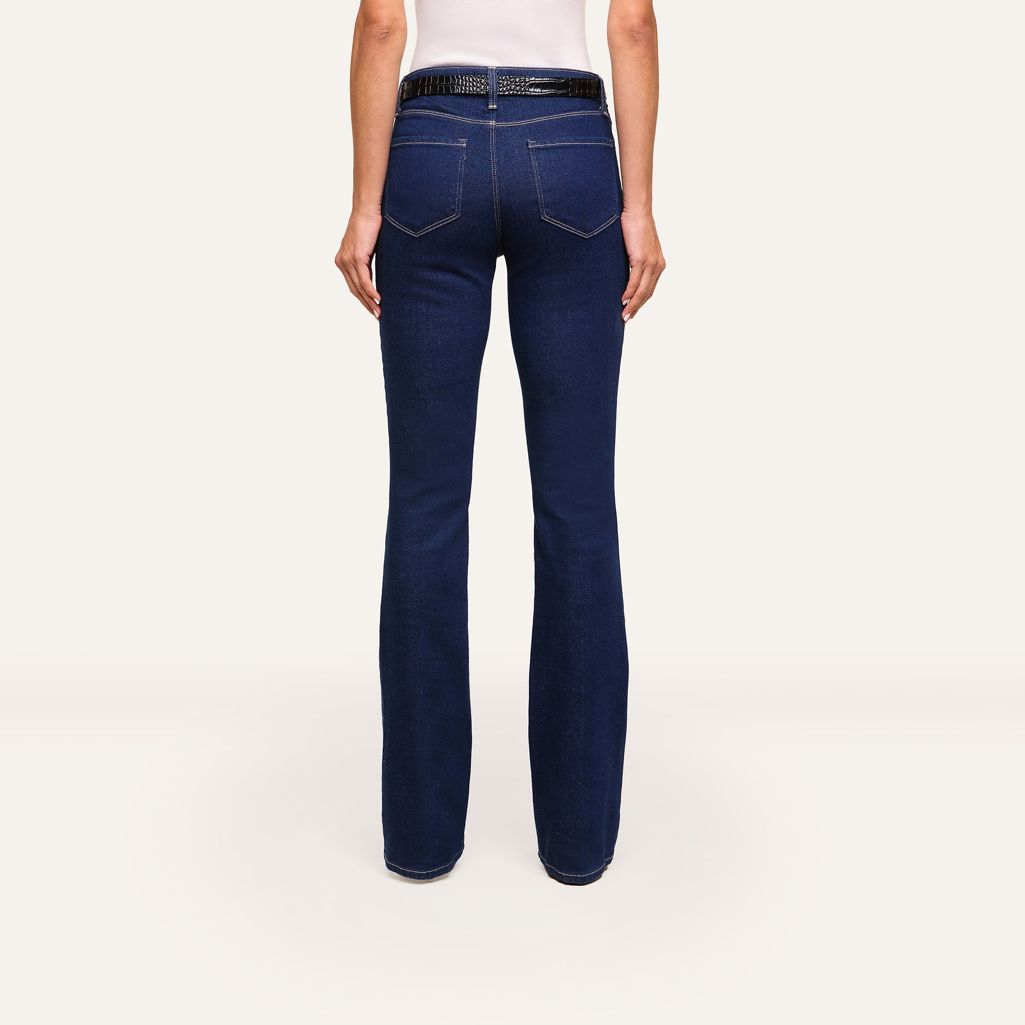 Person wearing Selma Bootcut Jean in dark blue stretch denim, paired with a black belt and white top, shown from the back against a plain white background.