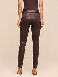 A person stands facing away against a plain white background, wearing a sleeveless brown top, the Jyothi Coated Jean in dark brown—featuring high-rise skinny fit with pockets and an ankle slit—a black belt, and tan high-heeled shoes.