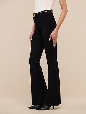 A person is shown from the shoulders down wearing the Marty Flare Pant in black, a white sleeveless top, black heels, and a black belt against a plain beige background.