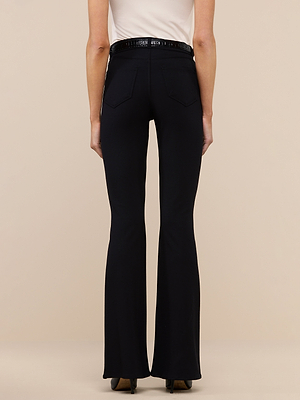 A person wearing a white sleeveless top and the black Marty Flare Pant with back pockets, seen from behind against a plain beige background.