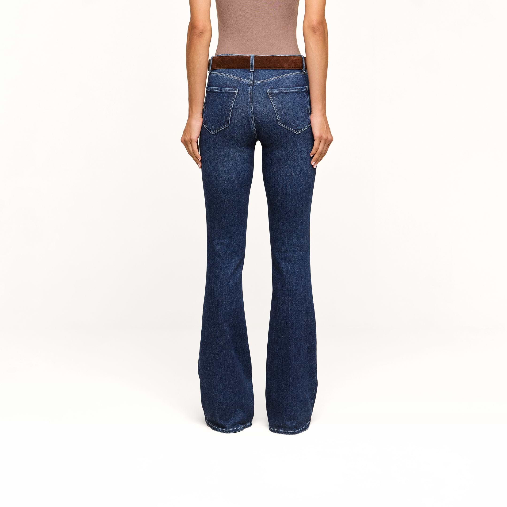 A person wearing a brown sleeveless top and the Marty Flare Jean in dark blue, viewed from the back, standing against a plain white background.