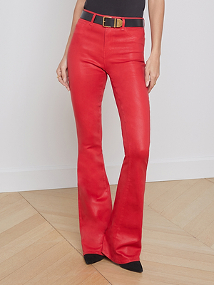 Wearing L'AGENCE Marty Coated Flare Jean in red, styled with a black belt and pointed-toe shoes. Only the lower torso and legs are visible, standing on a wooden floor against a light wall.