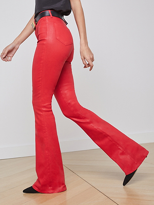 A person in a black top and shoes wears L'AGENCE's Marty Coated Flare Jean, bright red high-rise flares, while walking on a light wooden floor with only their lower half visible against a plain white wall.