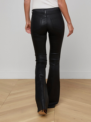 A person stands on a wooden floor, shown from the back, wearing the Marty Coated Flare Jean and a white top. These black jeans feature two back pockets, leg seams, and offer a chic leather alternative style.