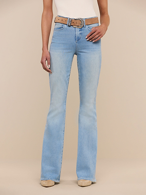 A person stands against a plain beige background, wearing the Marty Flare Jean in high rise light blue super stretch denim, paired with a beige belt, white top, and beige shoes. Photo cropped from shoulders down.
