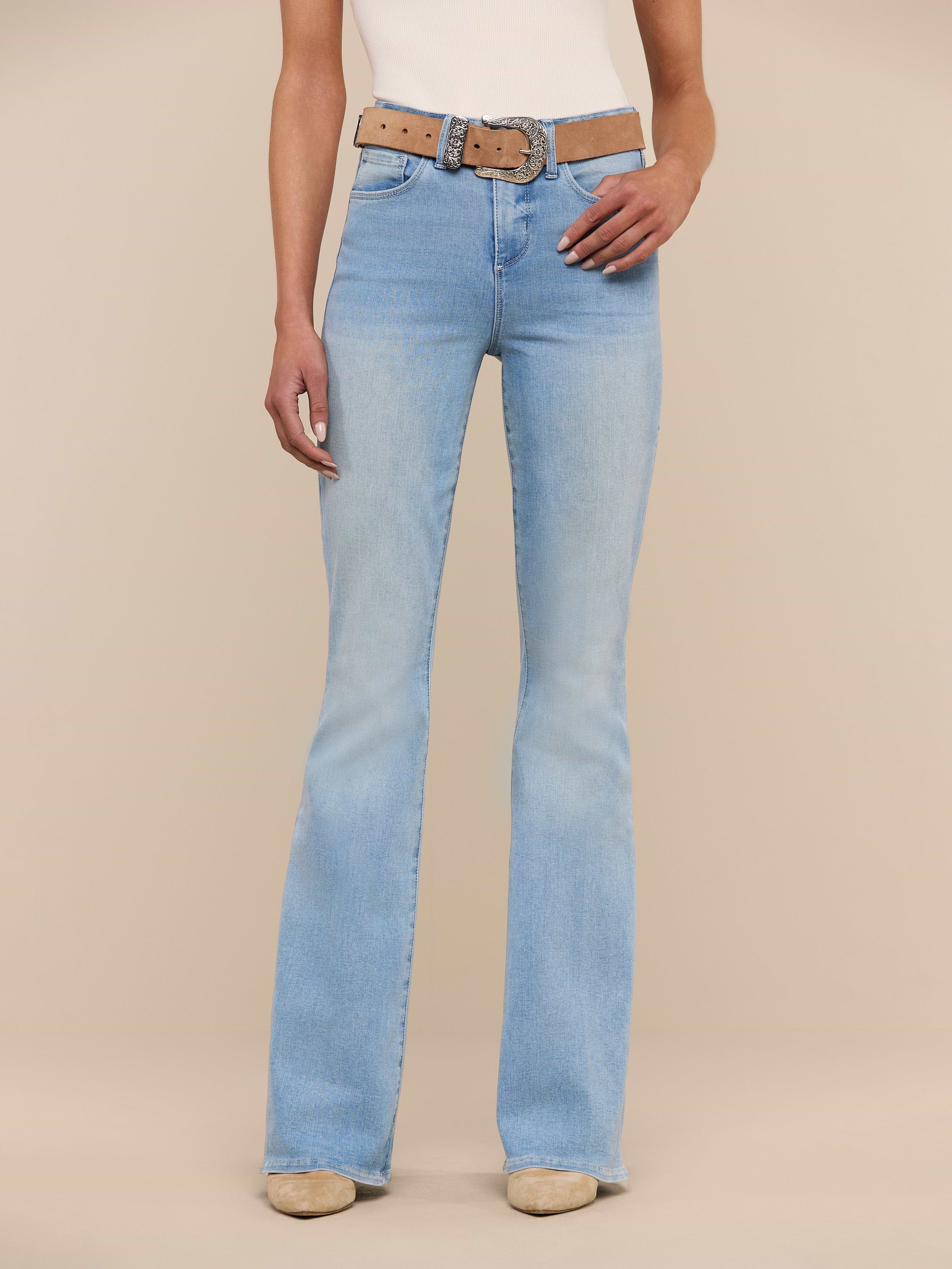 A person wearing Marty Flare Jean in light blue—a high rise, flare-leg style crafted from super stretch denim—paired with a tan belt, beige shoes, and a sleeveless top stands against a plain white background. Only the lower torso and legs are visible.