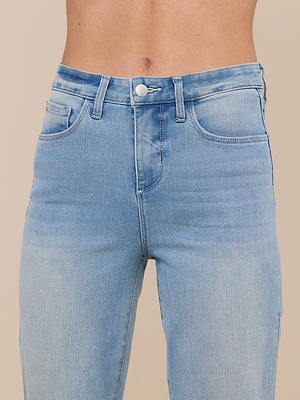 A close-up of a person wearing the Marty Flare Jean, featuring high rise light blue denim with visible waistband, button, zipper, and front pockets against a neutral background.