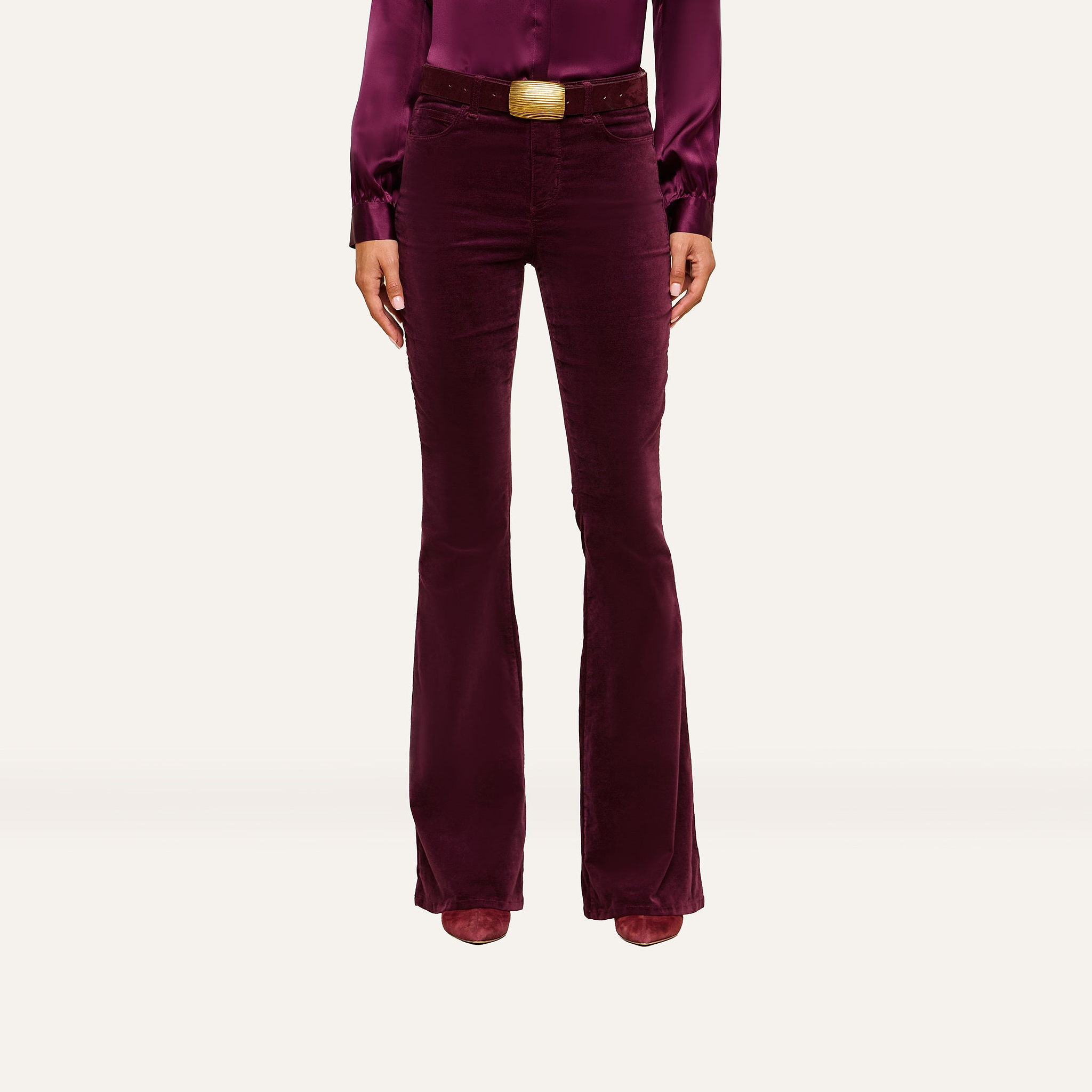 A person wearing a long-sleeved, burgundy blouse tucked into matching high-rise Marty Velvet Pants with a wide belt, standing against a plain background.