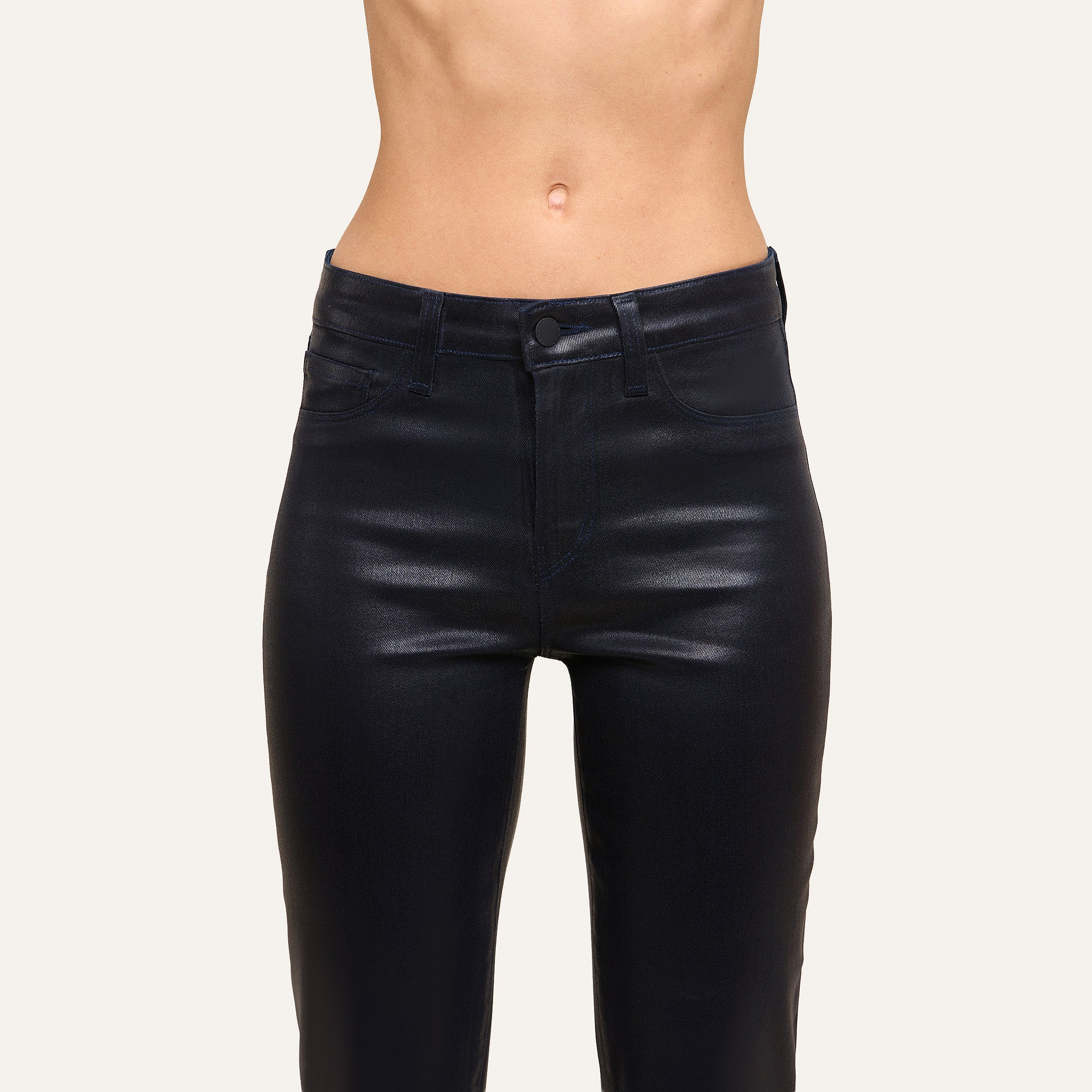 A person wearing Kendra Coated Cropped Flare Jean in shiny black stands against a plain light background, shown from mid-torso to upper thighs.