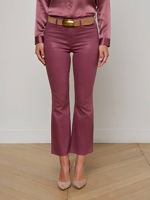 A person wearing Kendra Coated Cropped Flare Jeans in mauve, a silky matching blouse, a tan belt with a large buckle, and beige pointed-toe heels stands on a wooden floor against a plain wall.