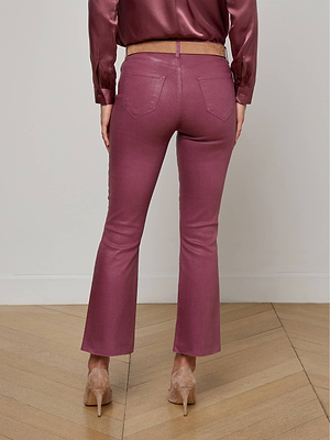A person stands facing away, wearing the Kendra Coated Cropped Flare Jean in mauve with a matching satin blouse and nude heels on a light wooden floor against a white wall.