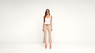 Woman stands against a plain white background wearing sunglasses, a white tank top, beige flared pants, a brown belt, and beige heels.