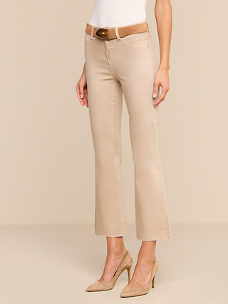A person wearing the Kendra Coated Cropped Flare Jean in beige, paired with a tan belt and matching tan high heels, stands against a neutral beige background. Only the lower torso and legs are visible.