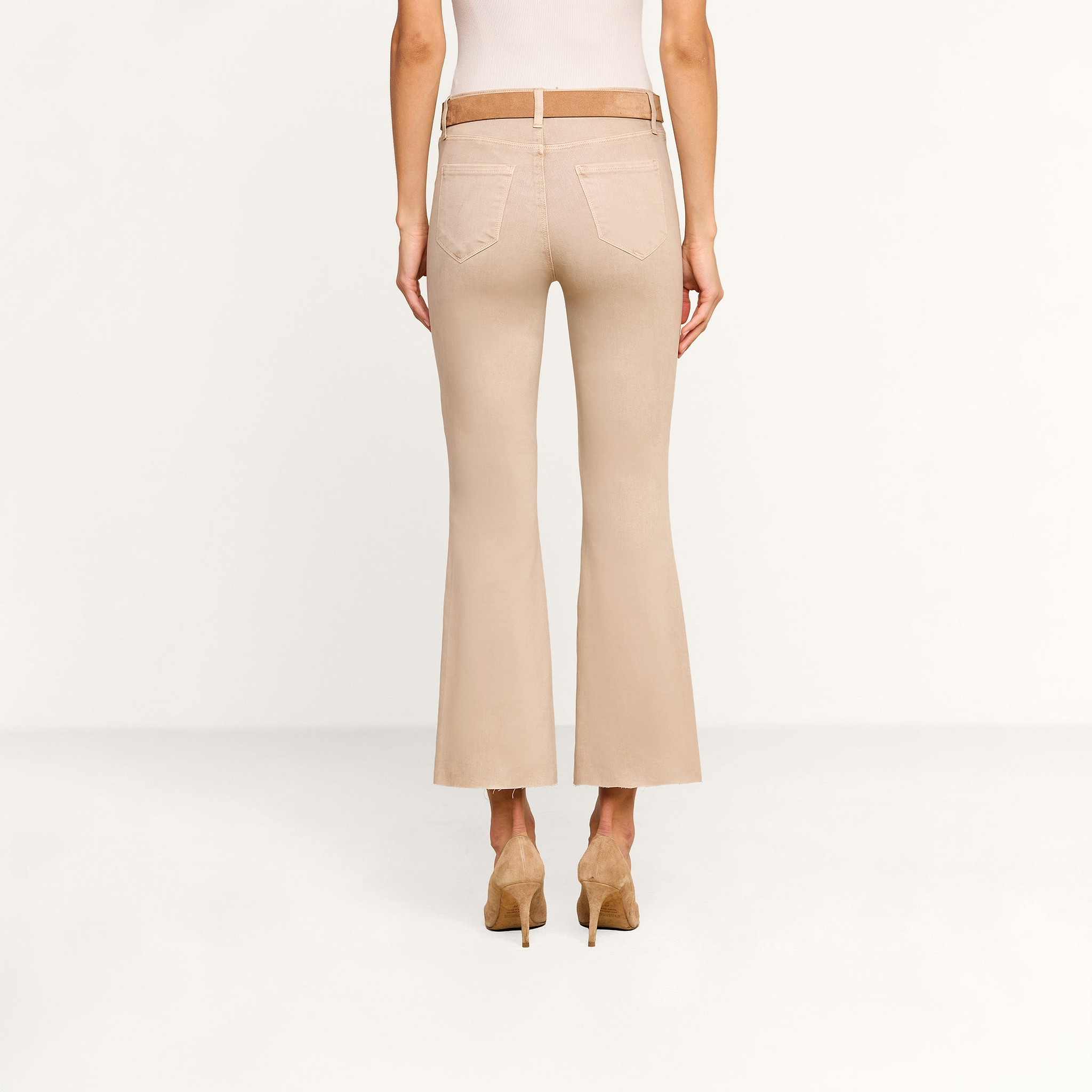A person wearing the Kendra Coated Cropped Flare Jean and tan high heels stands facing away in a plain, light-colored room.