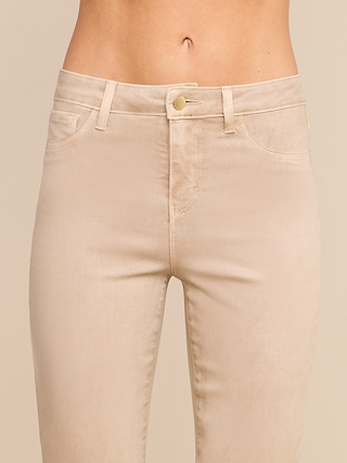 A close-up of a person wearing the Kendra Coated Cropped Flare Jean in beige, featuring a high rise, button and zipper closure, front pockets, and belt loops. The background is plain and neutral.