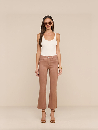 A woman stands facing forward against a beige background wearing sunglasses, a white sleeveless top, heeled sandals, and the Petite Kendra Coated Jean in a tan high rise cropped style.