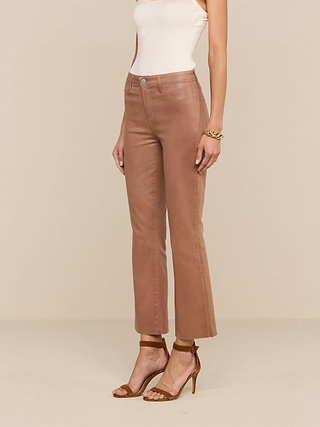 A woman stands against a neutral background wearing the Petite Kendra Coated Jean in tan, paired with a sleeveless white top, brown heeled sandals, and a gold bracelet.