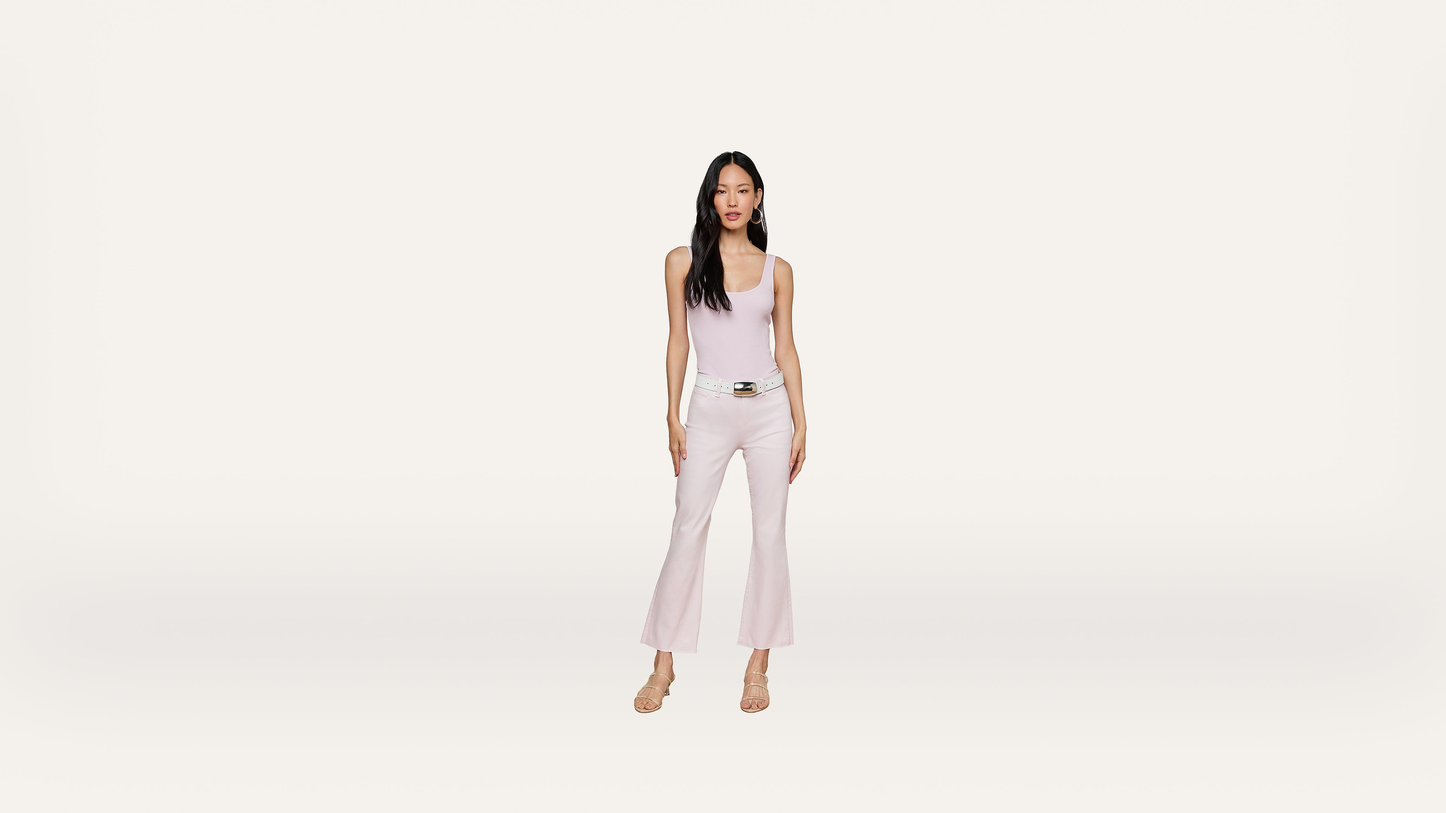 A woman stands facing forward, wearing a light pink sleeveless top, matching flared pants, and beige heels against a plain white background.