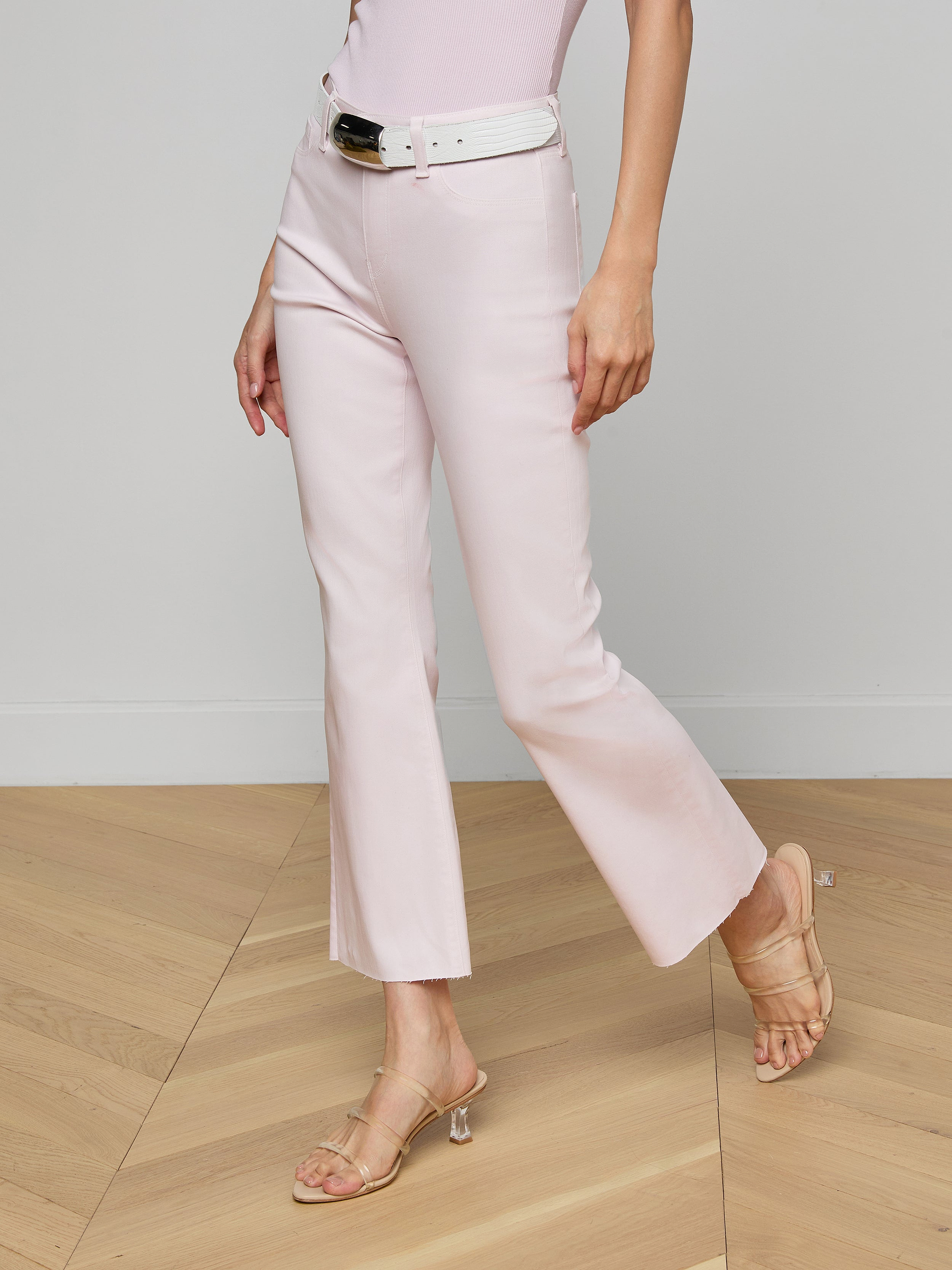 A person wearing the Kendra Coated Cropped Flare Jean in light pink, styled with a white belt, nude heeled sandals, and a matching light pink top against a plain background. Their face is not visible.