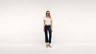 A woman wearing sunglasses, a white t-shirt, navy pants, a belt, and beige heels stands confidently against a plain white background.