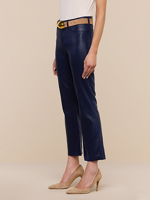 Someone stands against a beige background wearing Kendra Coated Cropped Flare Jeans in navy blue, styled with a white top, tan belt with a gold buckle, and tan suede high heels.