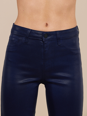 A close-up shows a person wearing the Kendra Coated Cropped Flare Jean in shiny dark blue, featuring a high-rise waist, front pockets, raw hem, and a glimpse of their midriff and navel.