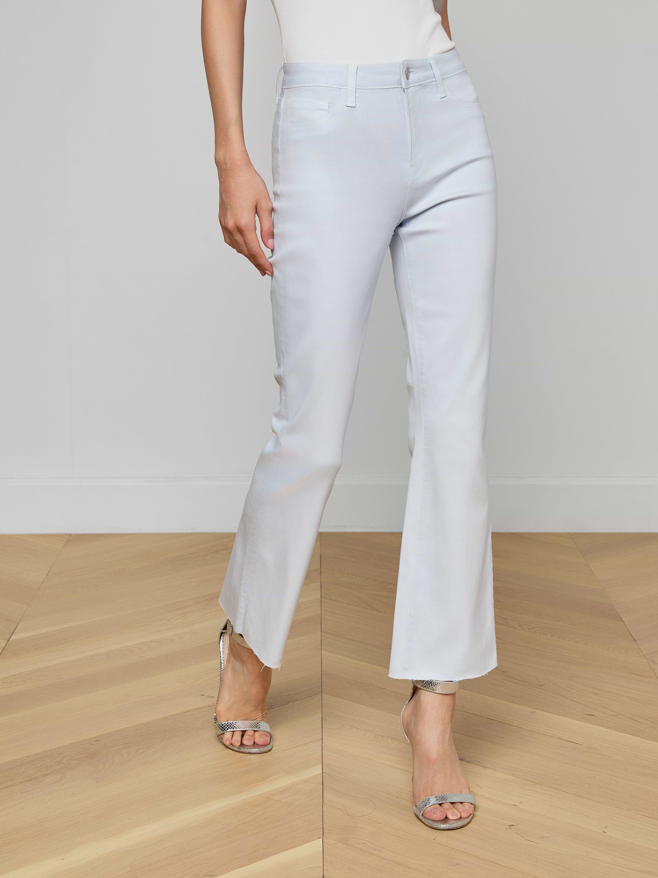 Someone wearing the Kendra Coated Cropped Flare Jean in light blue with silver heeled sandals stands on a wooden floor against a plain white wall, showing only the lower half of their body.