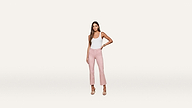 A woman stands against a white background, wearing a white sleeveless top paired with pink high-waisted cropped pants and nude heels. She has long hair and her left hand rests confidently on her hip, creating a chic, modern look.