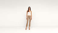 A woman wearing sunglasses, a white tank top, beige pants, and heeled sandals stands confidently against a plain white background.