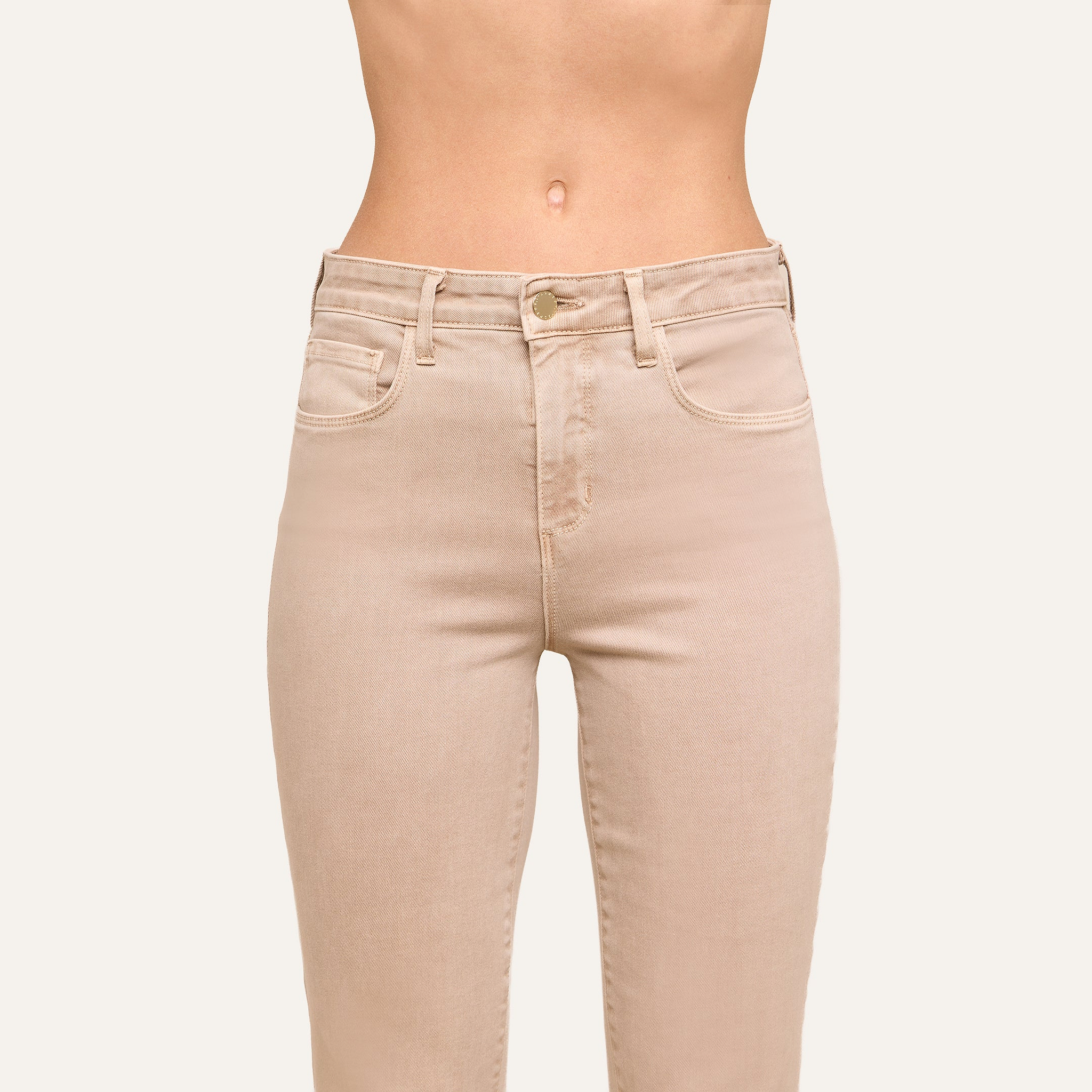 Wearing the Kendra Cropped Flare Jean in a high-waisted, neutral tan super stretch denim, this person stands against a plain light background showing only the torso and upper legs.