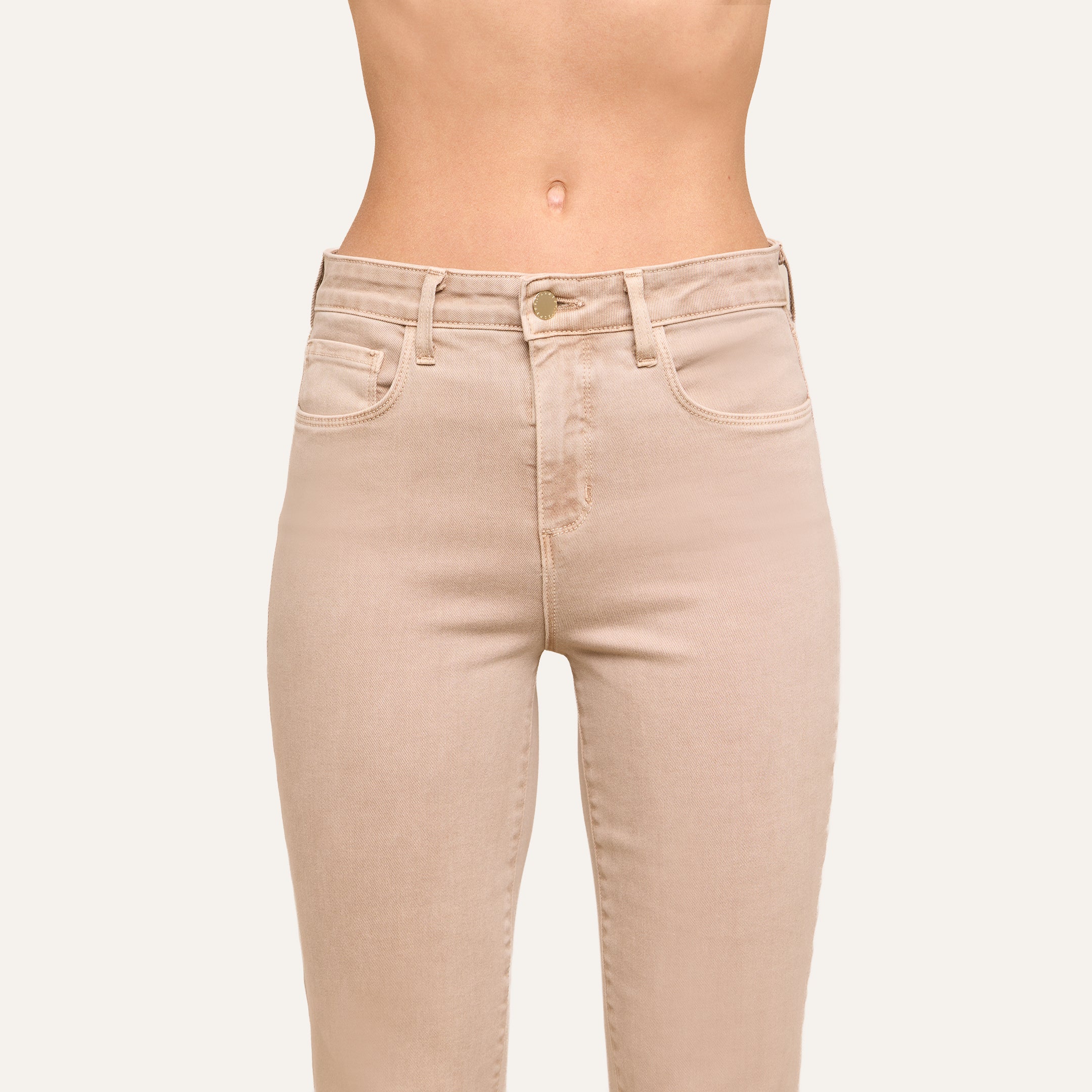Wearing the Kendra Cropped Flare Jean in a high-waisted, neutral tan super stretch denim, this person stands against a plain light background showing only the torso and upper legs.