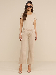 Una donna dai lunghi capelli castani, con indosso occhiali da sole, una maglietta a maniche corte color beige neutro, i jeans Wanda Cropped Wide-Leg e tacchi color carne, è in posa davanti a uno sfondo beige a tinta unita.