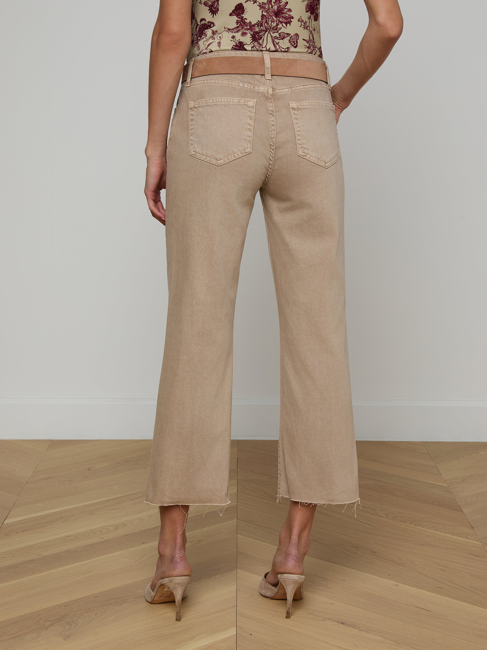 A person wearing Wanda Cropped Wide-Leg Jeans in a neutral tan color and heeled sandals, shown from the back, standing against a plain white background.