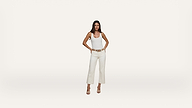 A woman stands facing forward with her hands on her hips, wearing a white tank top, white pants, and beige heels against a plain white background.