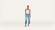 A person stands facing forward, wearing a white tank top, light blue high-waisted jeans, and beige heeled sandals against a plain white background.