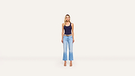 A woman stands facing forward in a navy tank top, light blue jeans, brown belt, and heels against a plain, light background, creating a casual yet polished look.