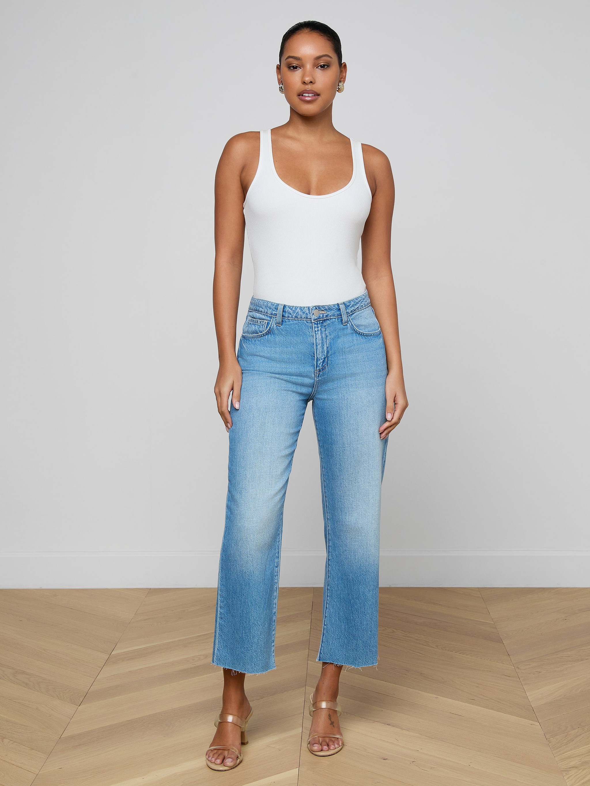 A woman stands against a plain background, wearing a white tank top, tan heeled sandals, and the Wanda Cropped Wide-Leg Jean in light blue all-cotton denim.