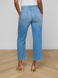 A person is seen from behind, standing against a plain white background, wearing the Wanda Cropped Wide-Leg Jean—light blue, high-waisted jeans crafted from 100 cotton denim—and beige heeled sandals.