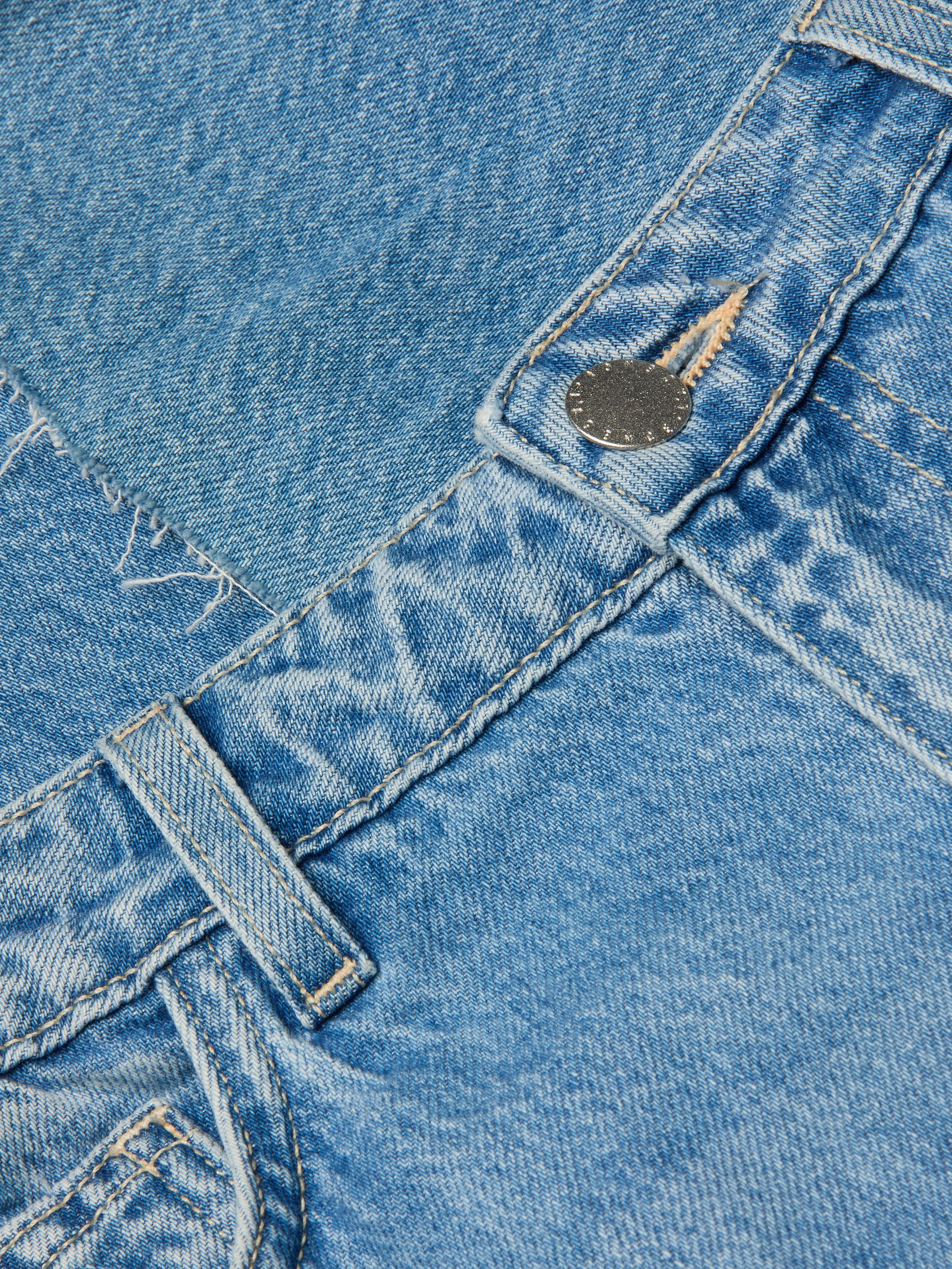 Close-up of the Wanda Cropped Wide-Leg Jean in light blue, crafted from 100 cotton denim, featuring a belt loop, metal button, visible stitching, and a pocket with frayed detailing.