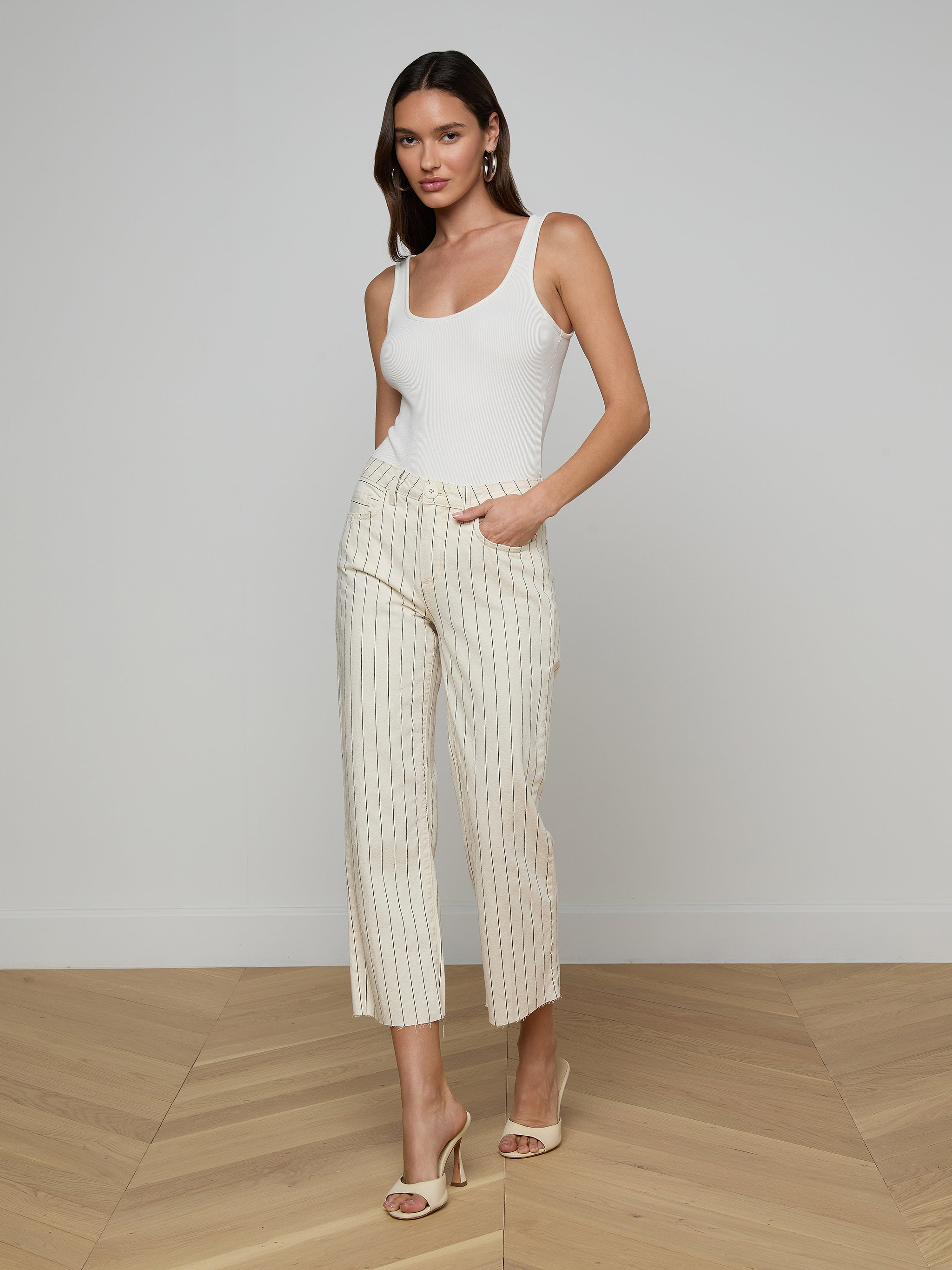 A woman wearing a white tank top, the Wanda Cropped Wide-Leg Pant with nautical stripes, and beige heeled sandals stands with one hand in her pocket against a plain white background.