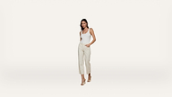 Woman wearing a white sleeveless top and light-colored, striped pants with beige high-heeled sandals, standing against a plain white background.