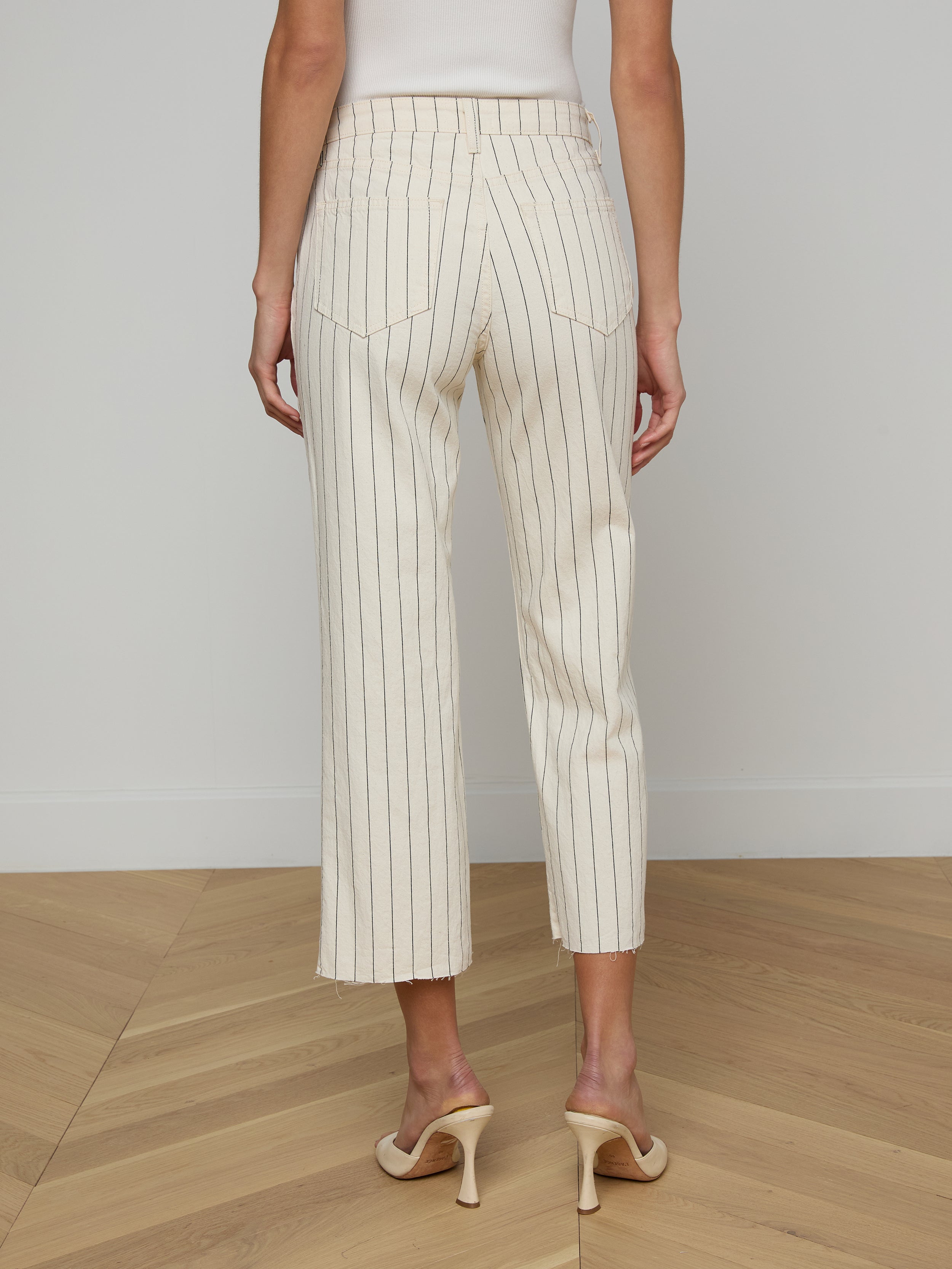 A woman stands facing away, wearing the Wanda Cropped Wide-Leg Pant in a cream nautical stripe and beige high heels against a plain background.