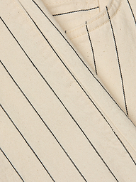 Close-up of the Wanda Cropped Wide-Leg Pant in beige cotton twill with black vertical pinstripes in a nautical stripe pattern, showing part of a seam and pocket. The texture of the fabric and stitching details are visible.