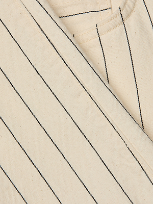 Close-up of the Wanda Cropped Wide-Leg Pant in cream-colored cotton twill with thin black vertical stripes, highlighting intersecting seams and a neatly finished edge.