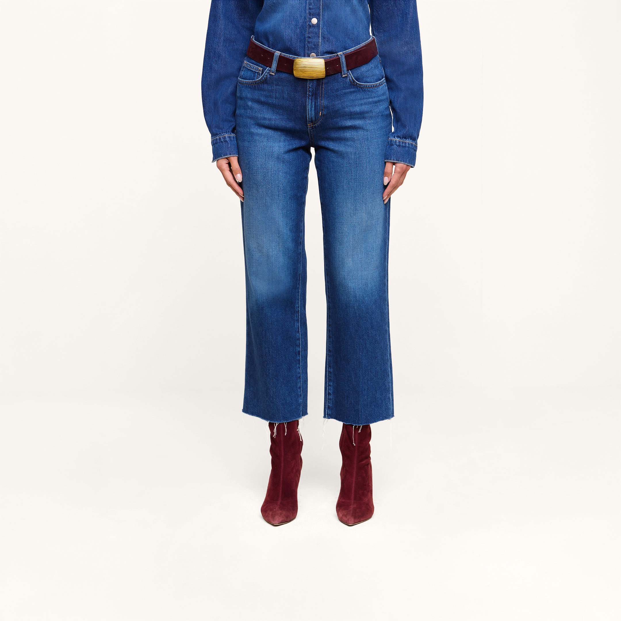 A person wearing a featherweight denim shirt, the Wanda Cropped Wide-Leg Jeans with a belt, and burgundy heeled boots stands against a plain white background.