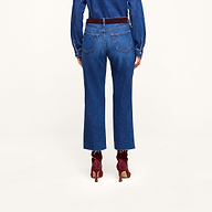A person standing facing away on a plain white background wears a long-sleeve featherweight denim shirt, the Wanda Cropped Wide-Leg Jean featuring high rise styling and back pockets, accented with a dark red belt and matching dark red heeled ankle boots.
