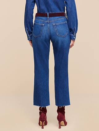Wearing the Wanda Cropped Wide-Leg Jean in blue, a blue long-sleeve shirt, a dark red belt, and red heeled boots, the person stands with their back to the camera against a beige background.
