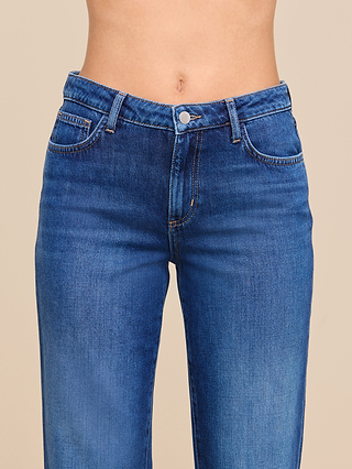 A close-up of a person wearing the Wanda Cropped Wide-Leg Jean, highlighting the high-rise waistband, button, and front pockets. The image is cropped at the midriff and upper thighs against a neutral beige background.
