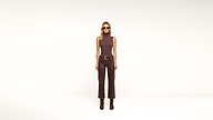 A woman wearing sunglasses, a sleeveless brown top, brown pants, and brown boots stands against a plain white background.