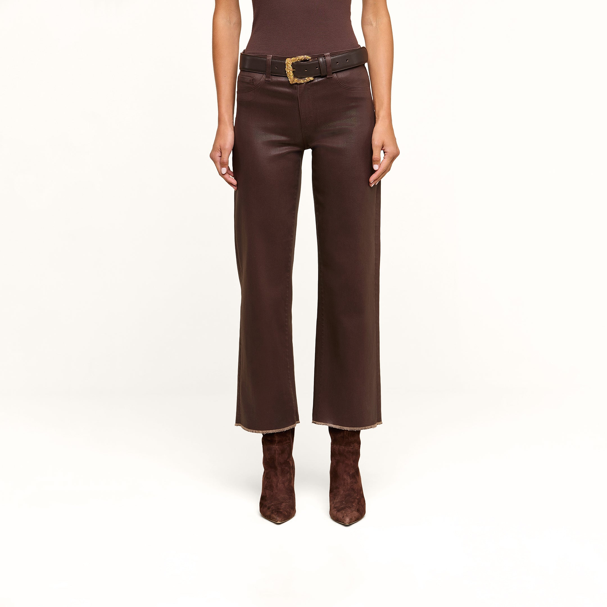 A person wearing the Wanda Coated Cropped Wide-Leg Jean with a black belt and brown suede boots, standing against a beige background.
